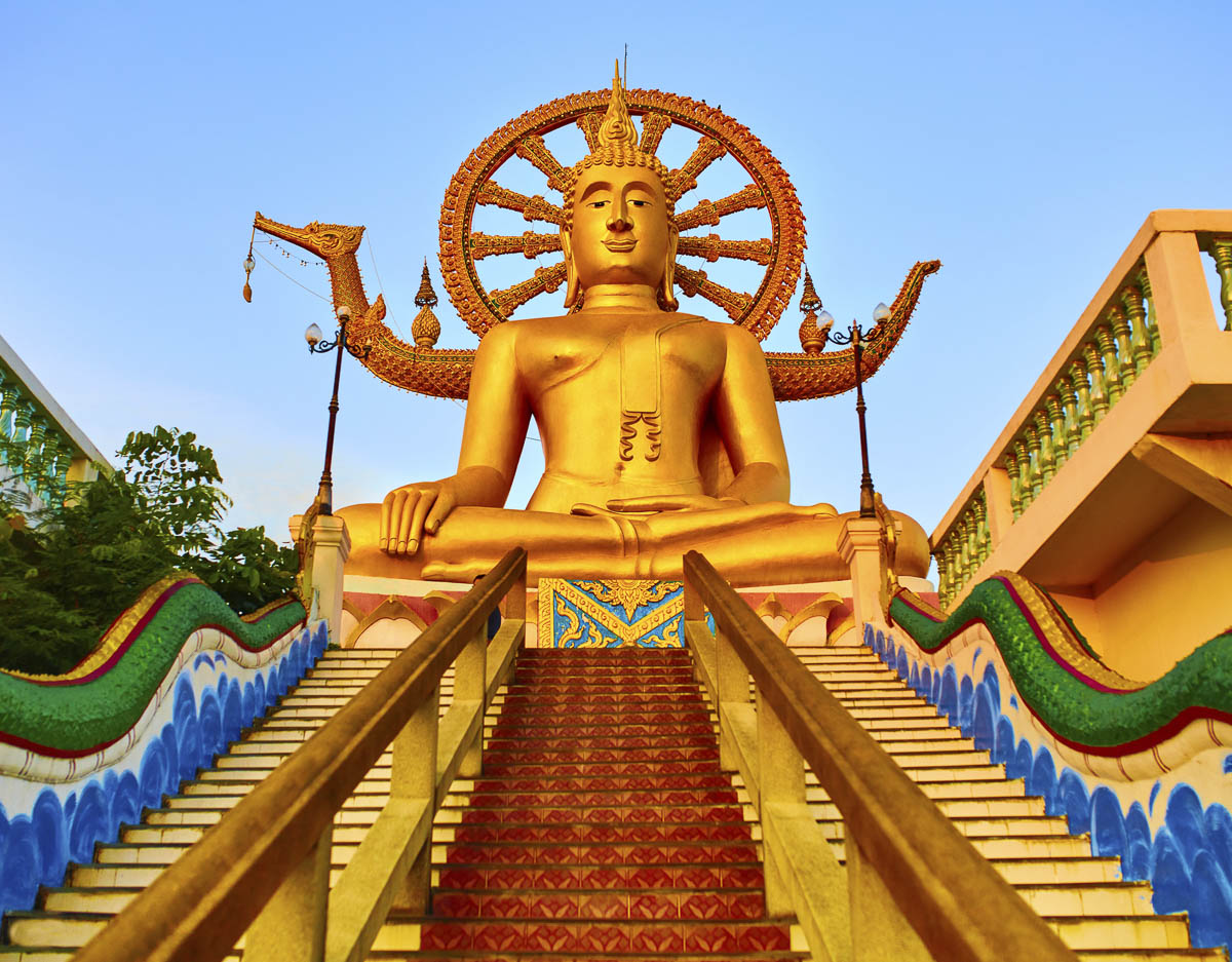 Estátua dourada do Grande Buda sentada no alto de uma escadaria com detalhes coloridos em Koh Samui.