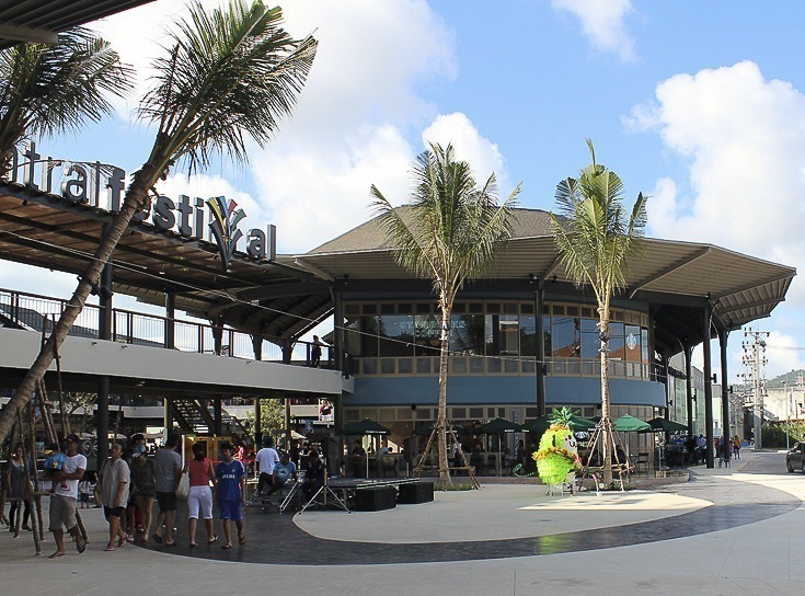 Entrada do shopping Central Festival em Koh Samui com pessoas caminhando e céu azul ao fundo.