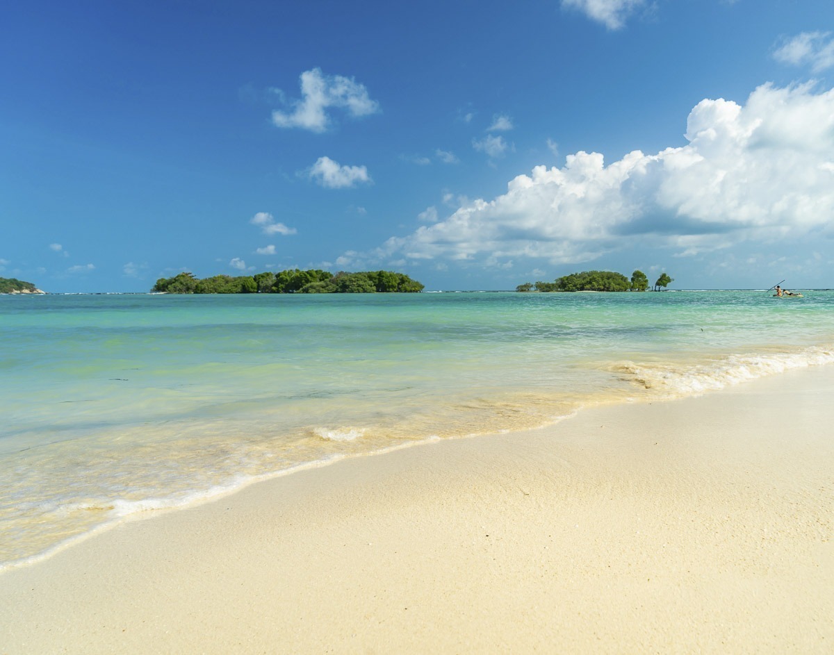 Praia de areia branca com mar turquesa em Koh Samui, com pequenas ilhas cobertas de vegetação ao fundo.