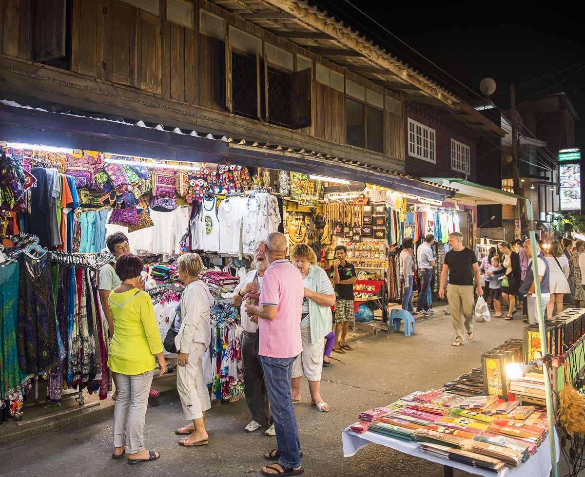Várias pessoas circulando e comprando roupas e artesanato em uma feira noturna iluminada em Koh Samui.