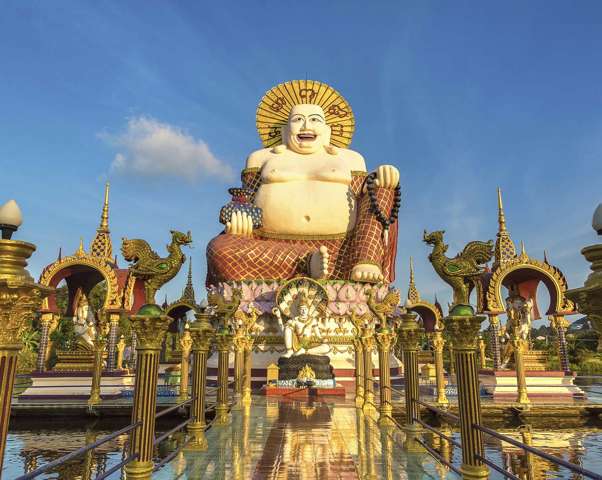 Estátua gigante do Buda Sorridente com túnica vermelha e colar de contas, cercada por esculturas douradas em Koh Samui.