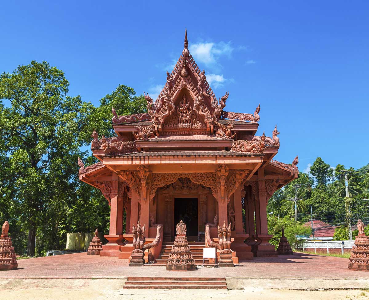 Templo tailandês inteiramente esculpido em tom de terracota com ornamentos detalhados e escadas com serpentes nagas.