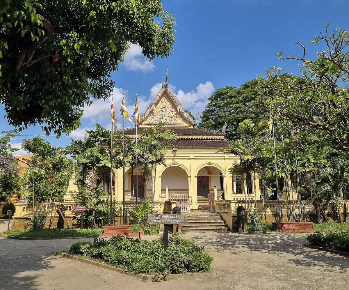 Entrada principal do templo Wat Damnak com jardim e bandeiras budistas.