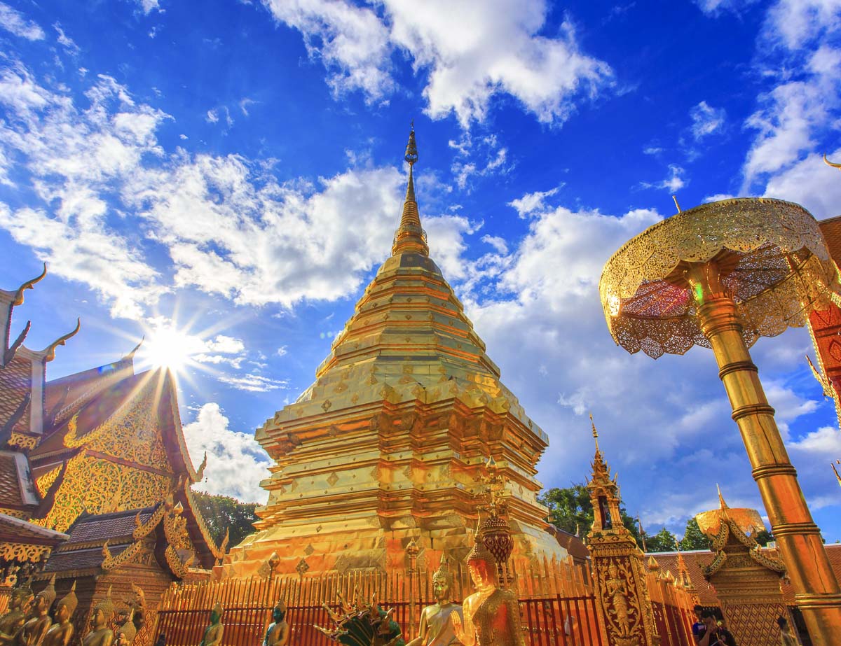 Estupa dourada do templo Wat Phra That Doi Suthep em Chiang Mai sob céu azul com nuvens e sol radiante.