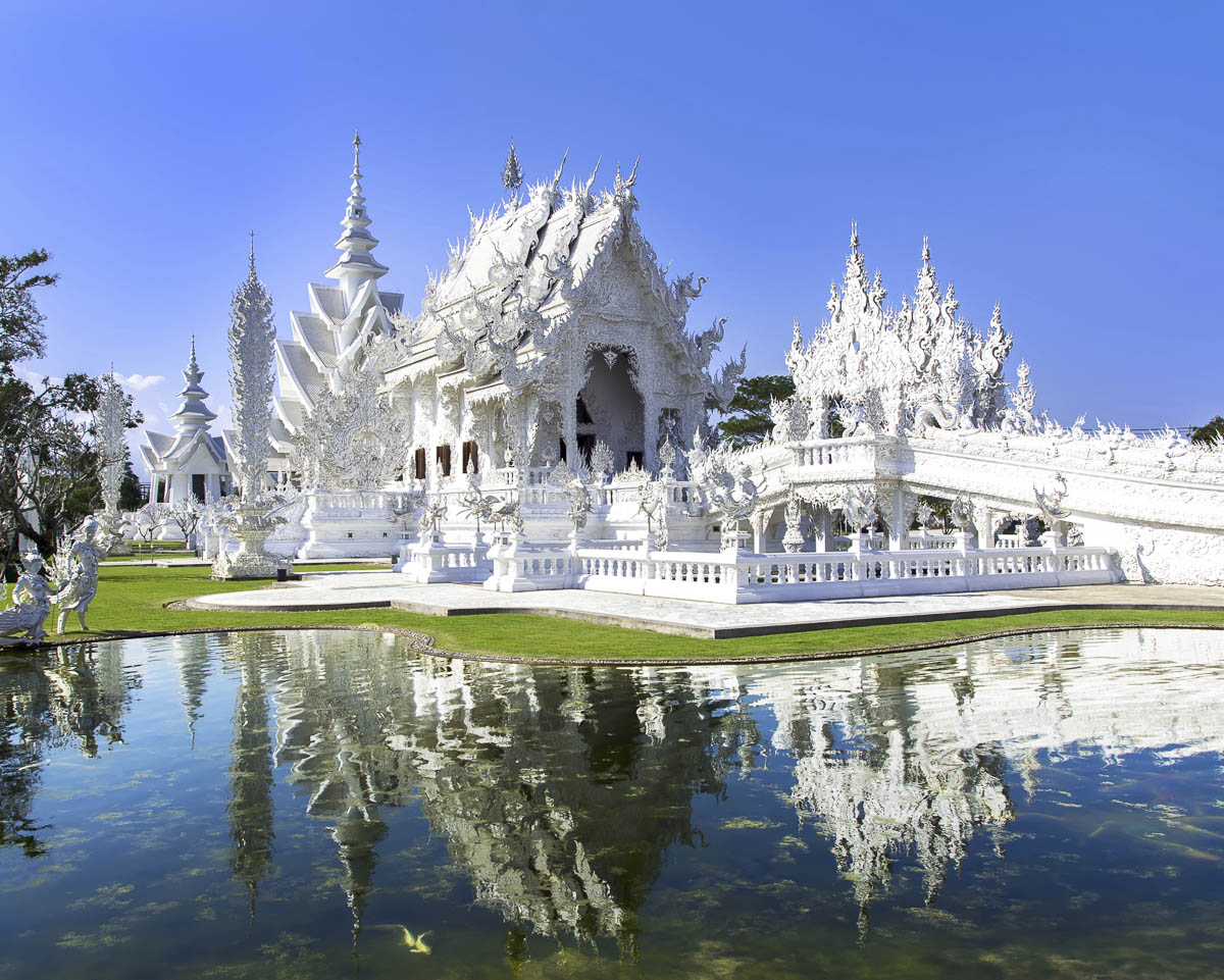 Templo Wat Rong Khun em Chiang Rai, com estrutura totalmente branca e ornamentação detalhada refletida em um lago em frente.