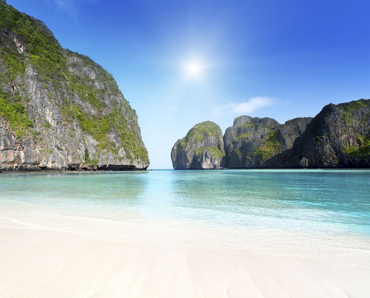 Praia de areia branca com águas transparentes cercada por falésias cobertas de vegetação em Maya Bay, Tailândia.