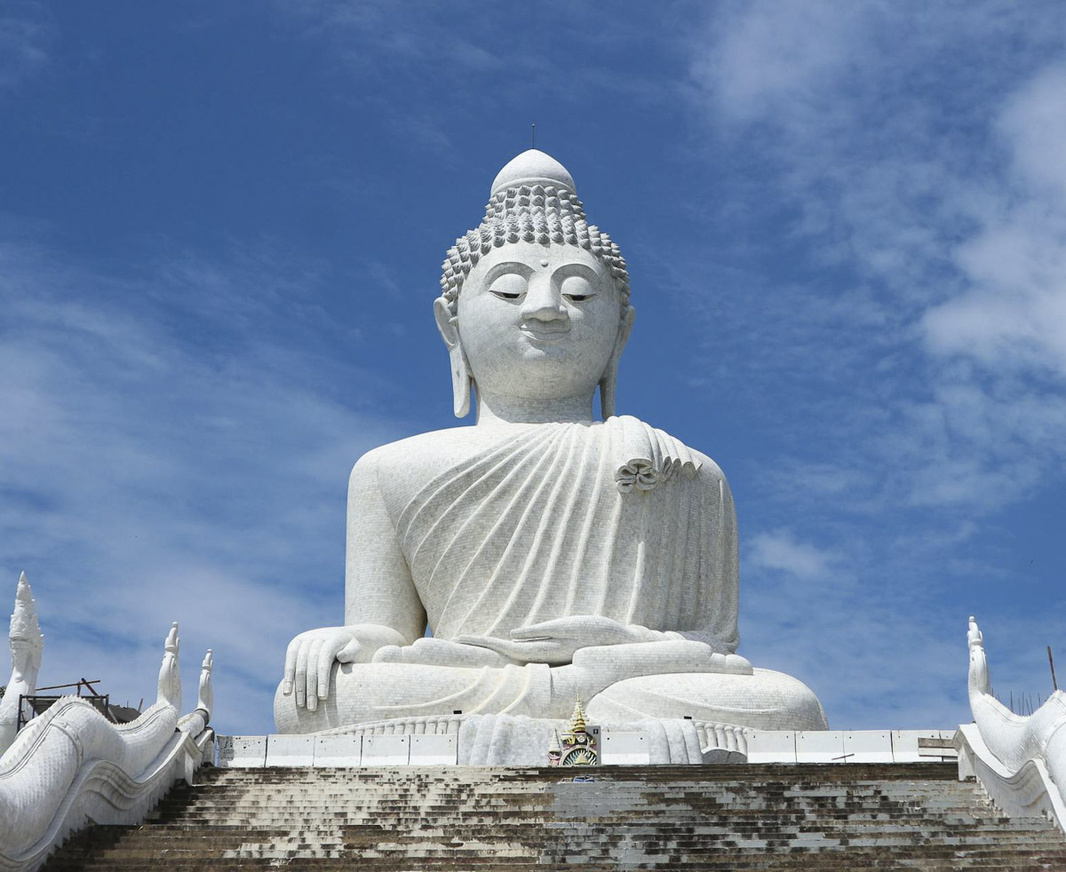 Estátua gigante de Buda branco sentada sobre uma escadaria, com céu azul ao fundo, em Phuket, Tailândia.