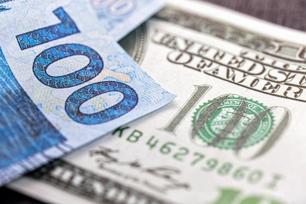 Notas de 100 reais e 100 dólares sobrepostas em close.