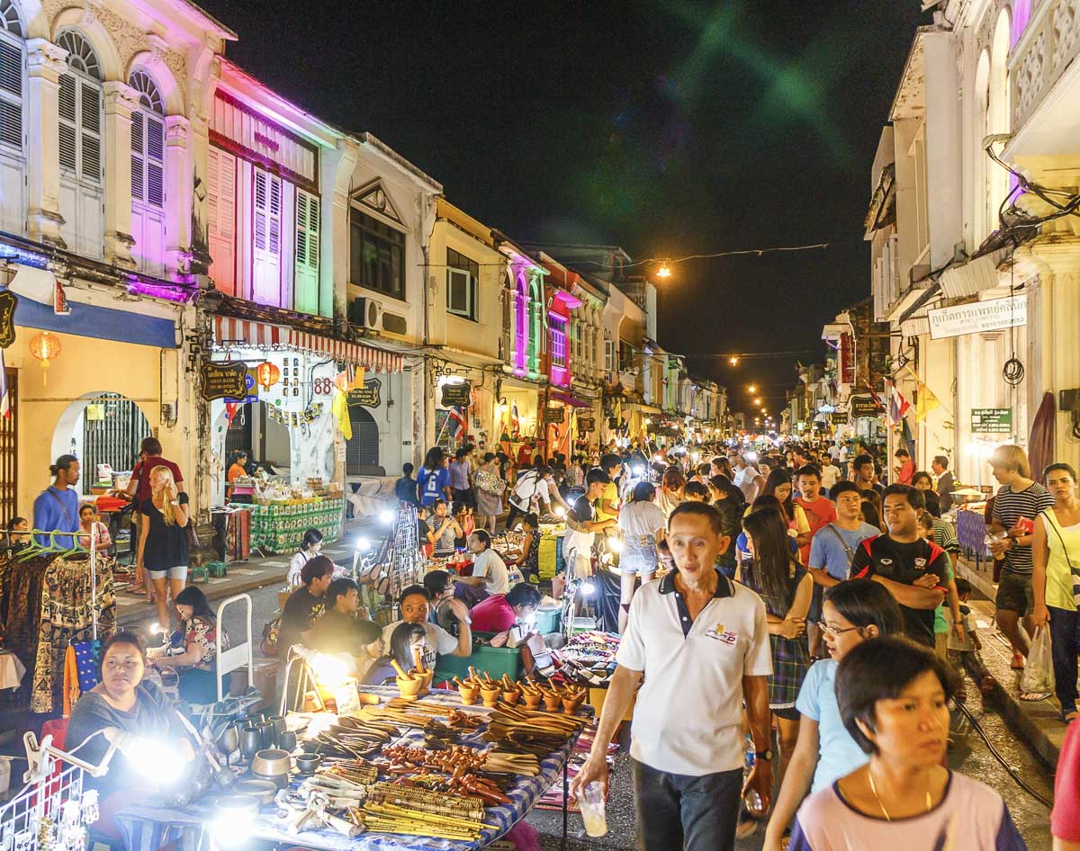 Feira noturna de rua na Tailândia com barracas iluminadas, vendedores e visitantes passeando entre lojas coloridas.
