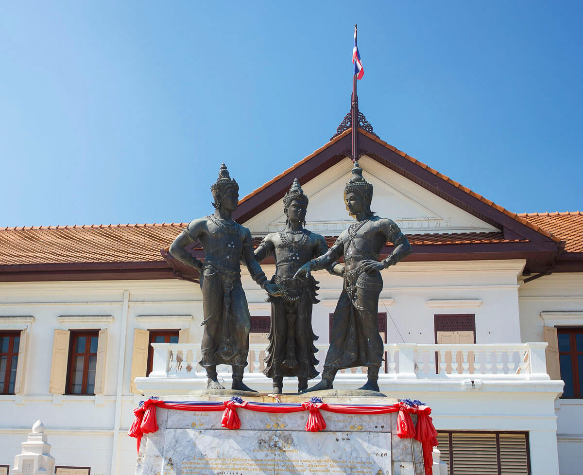 O Three Kings Monument em frente a um prédio branco de telhado laranja em Chiang Mai.