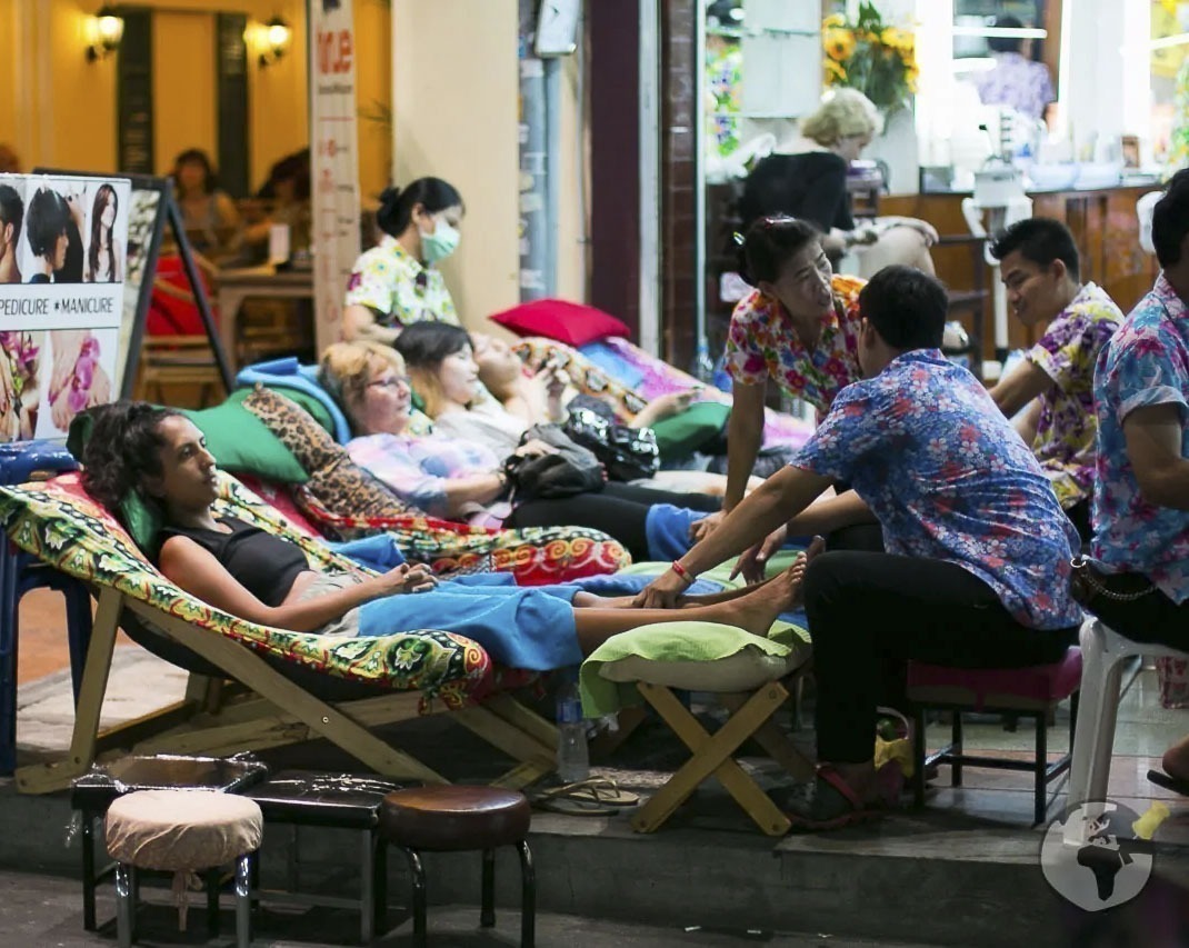 Pessoas relaxam em espreguiçadeiras recebendo massagem tailandesa em calçada movimentada de Chiang Mai.