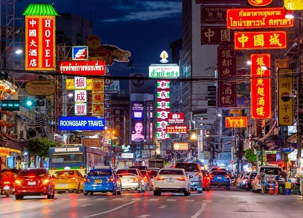 Ruas agitadas de Chinatown em Bangkok com letreiros coloridos e tráfego à noite.