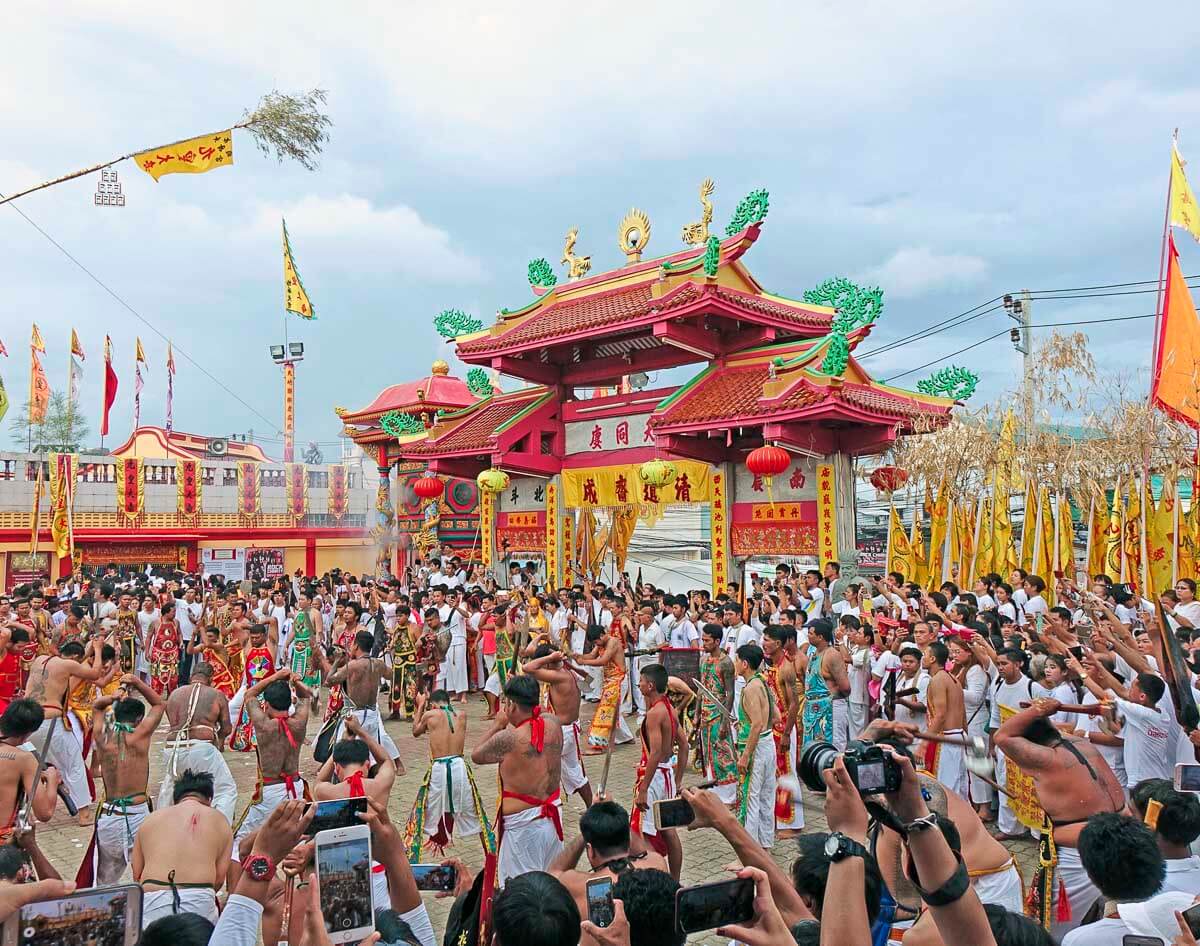 Cerimônia do Festival Vegetariano de Phuket com devotos vestidos de branco e praticando rituais em frente a um templo chinês.