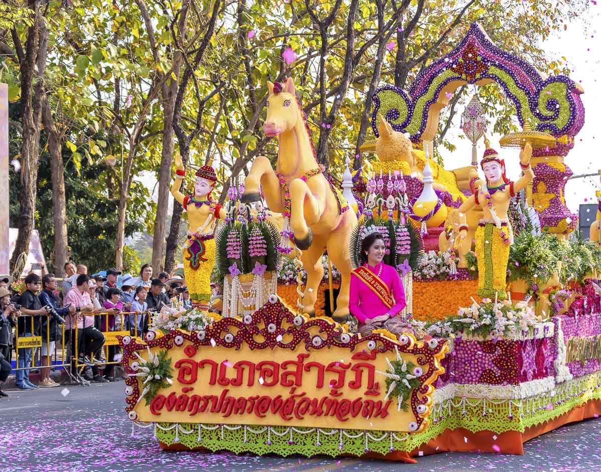 Carro alegórico com esculturas florais amarelas e dançarinos tradicionais no Festival das Flores de Chiang Mai.