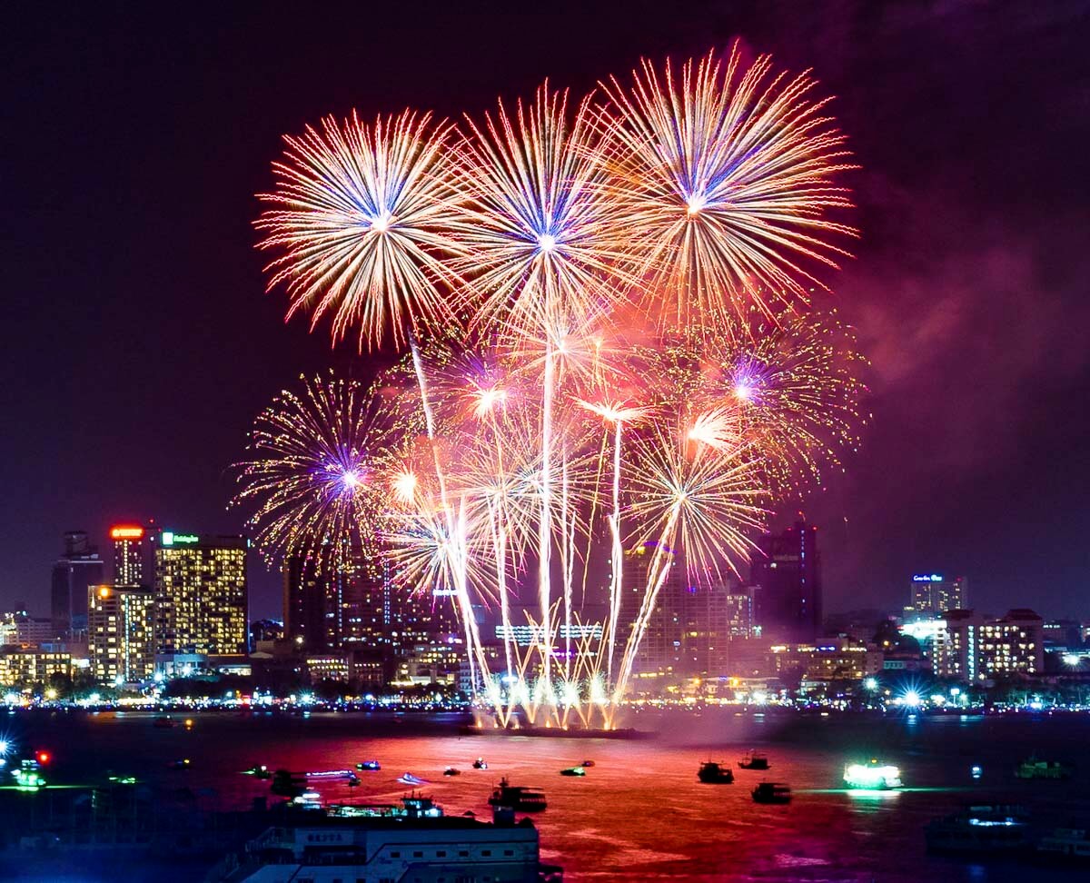 Fogos de artifício coloridos iluminando o céu sobre o mar e os prédios de Pattaya à noite.