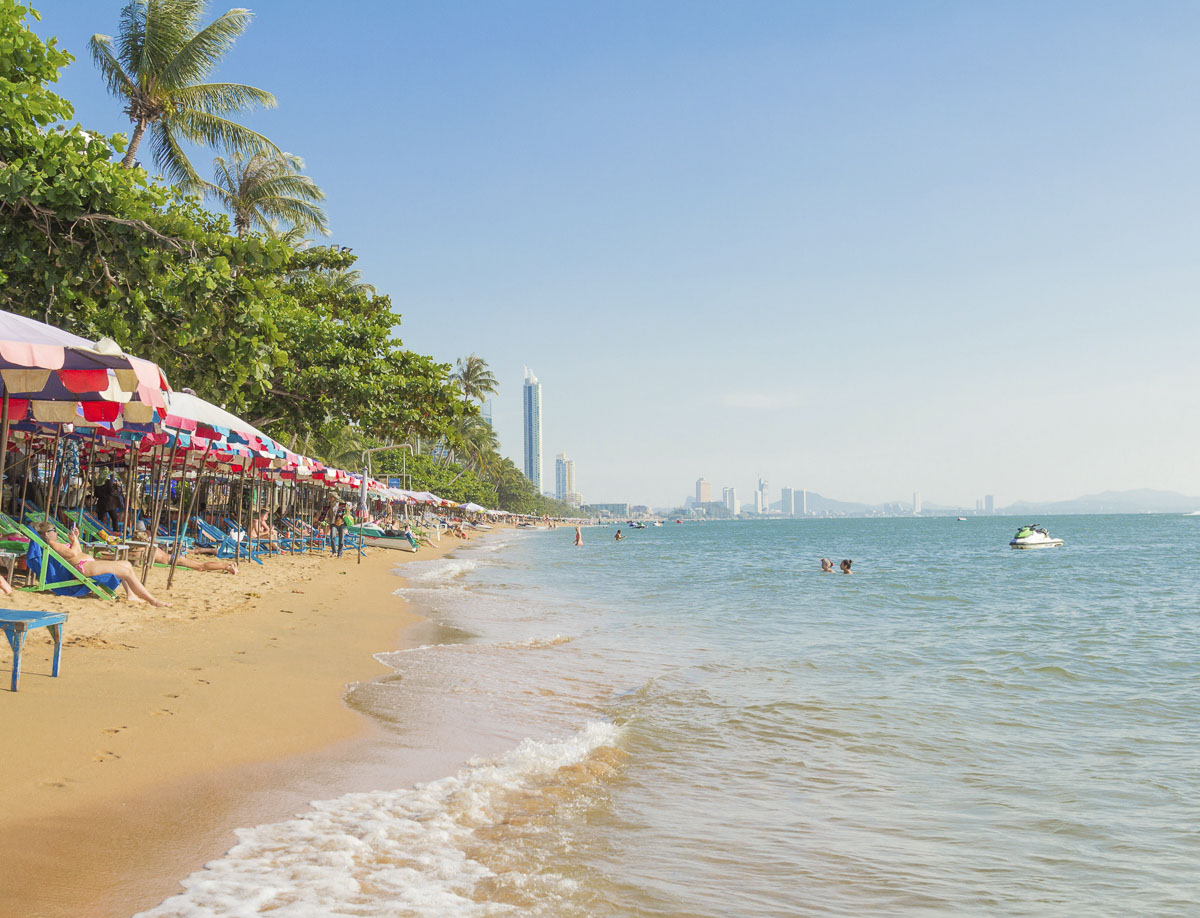 Praia de Jomtien com guarda-sóis coloridos, areia dourada e mar calmo em Pattaya.