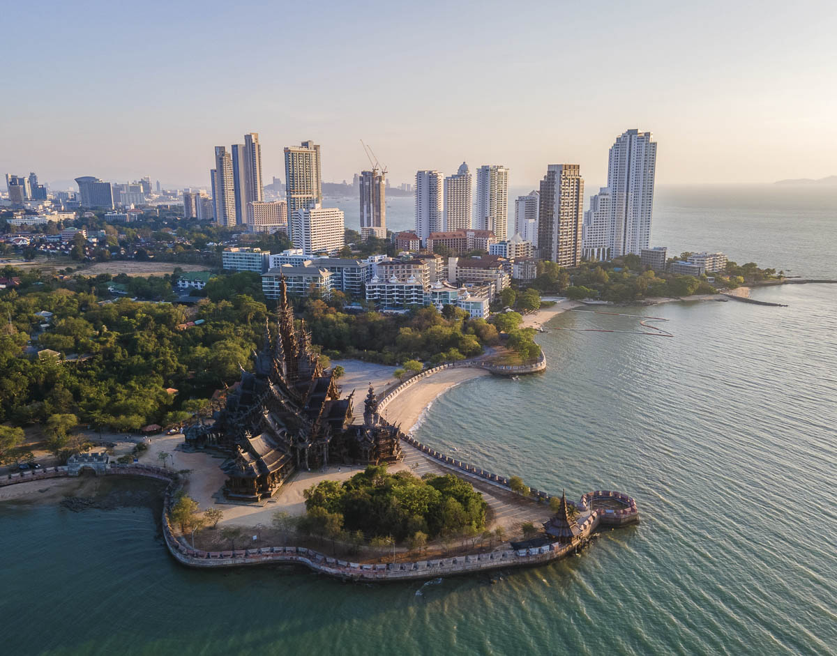 Vista aérea do Santuário da Verdade à beira-mar com prédios modernos de Pattaya ao fundo.