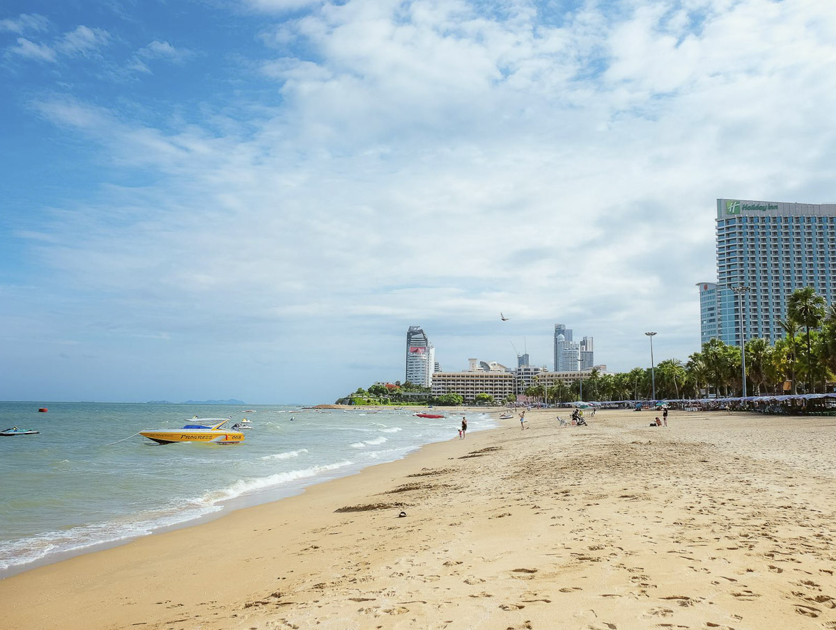 Praia central de Pattaya com areia dourada, mar calmo e hotéis ao fundo.