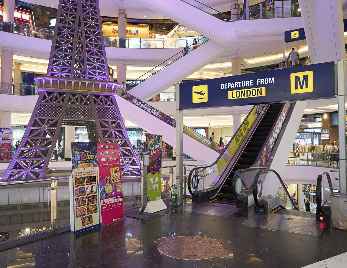 Interior do shopping Terminal 21 Pattaya com escada rolante e réplica iluminada da Torre Eiffel.