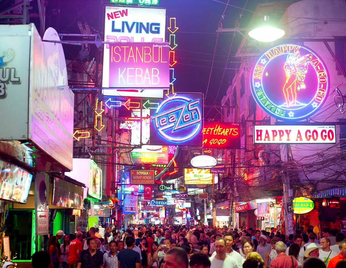 Rua movimentada de Pattaya à noite com letreiros coloridos de néon e grande fluxo de pessoas.