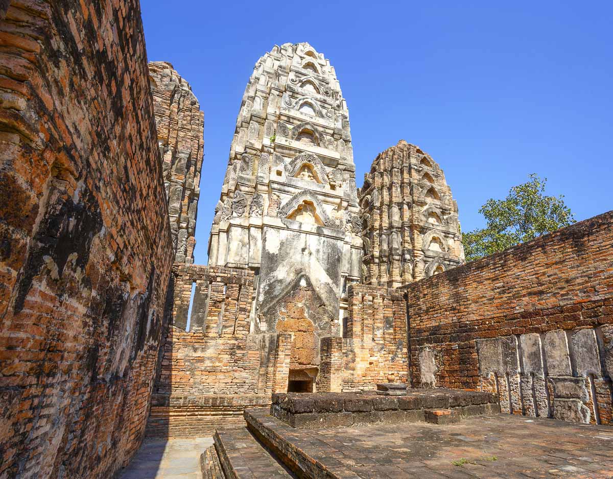 Três torres do templo Wat Si Sawai, em Sukhothai, vistas de frente sob o céu azul.