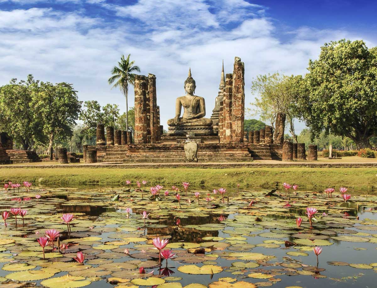 Grande estátua de Buda sentada cercada por lago com flores de lótus no Wat Mahathat, em Sukhothai.