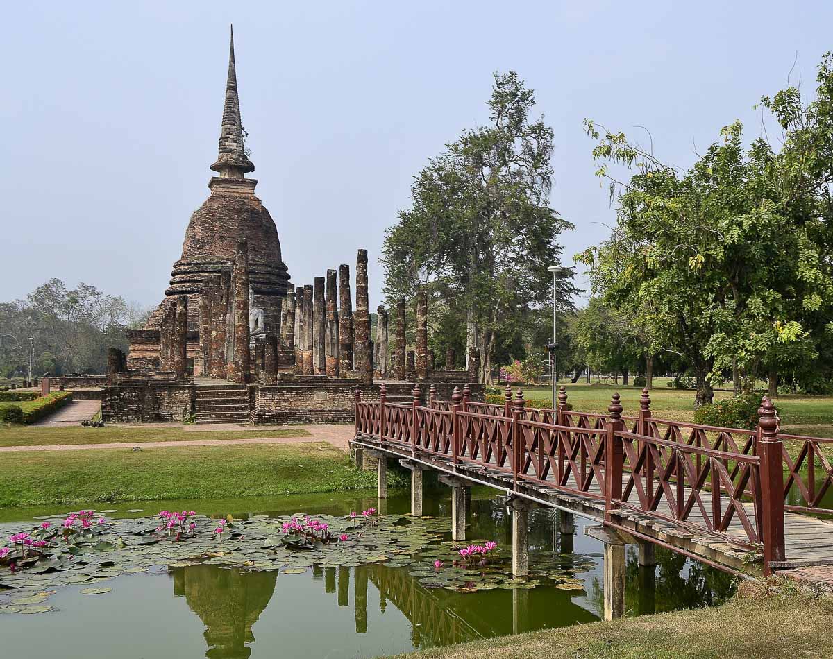 Templo Wat Sa Si com chedi cercado por colunas e lago com flores de lótus em Sukhothai.