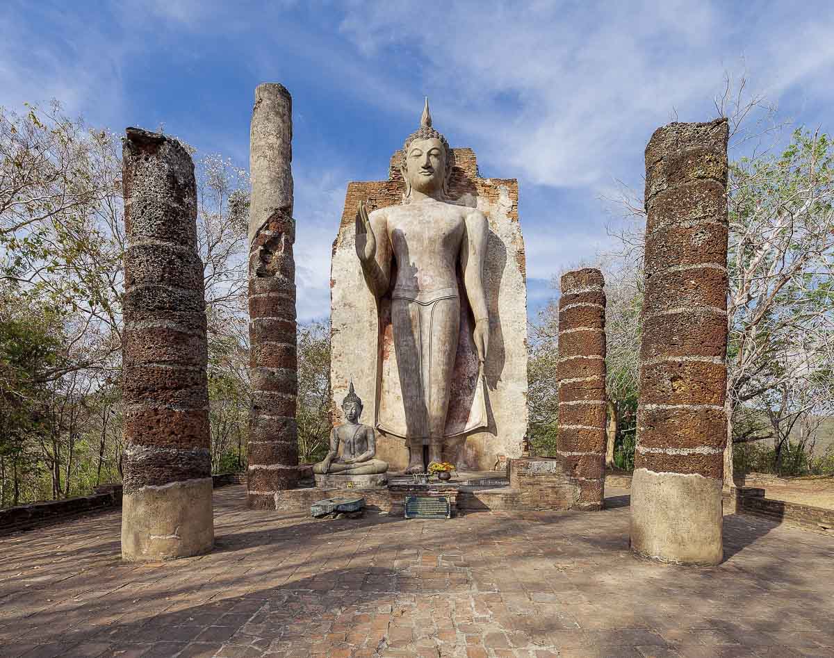Estátua alta de Buda em pé cercada por colunas antigas no alto de uma colina em Sukhothai.