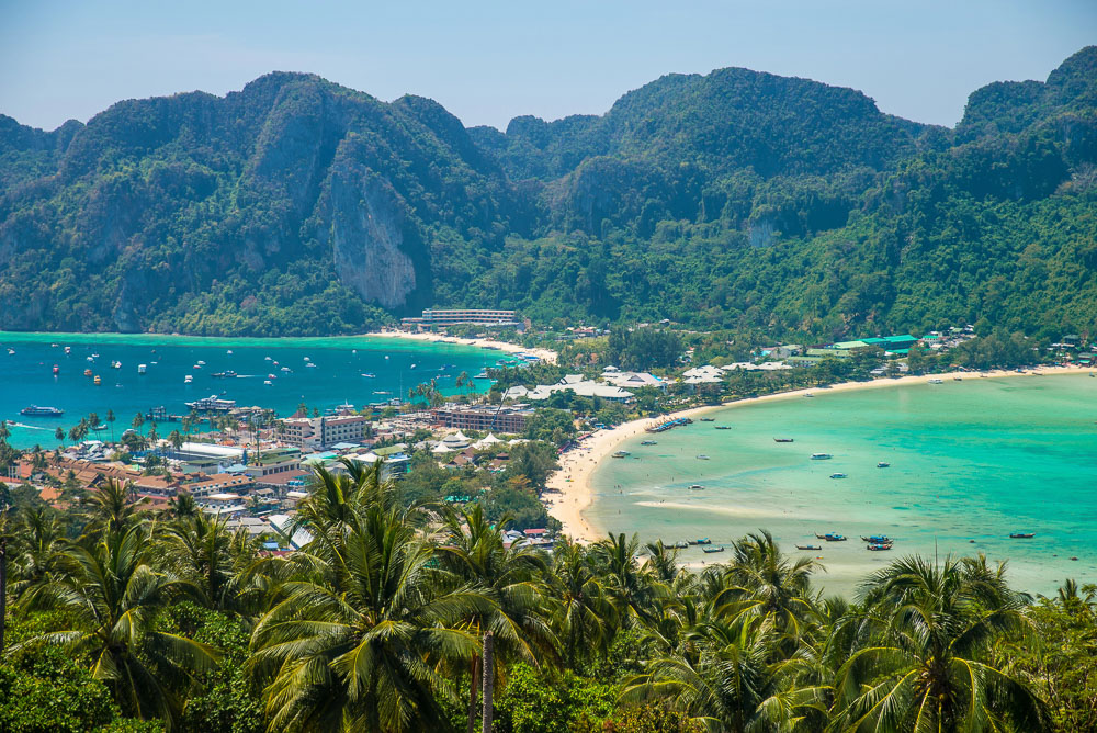 Enseadas em tons de azul e verde cercam o centro urbano da Ilha Phi Phi com vegetação tropical ao redor.