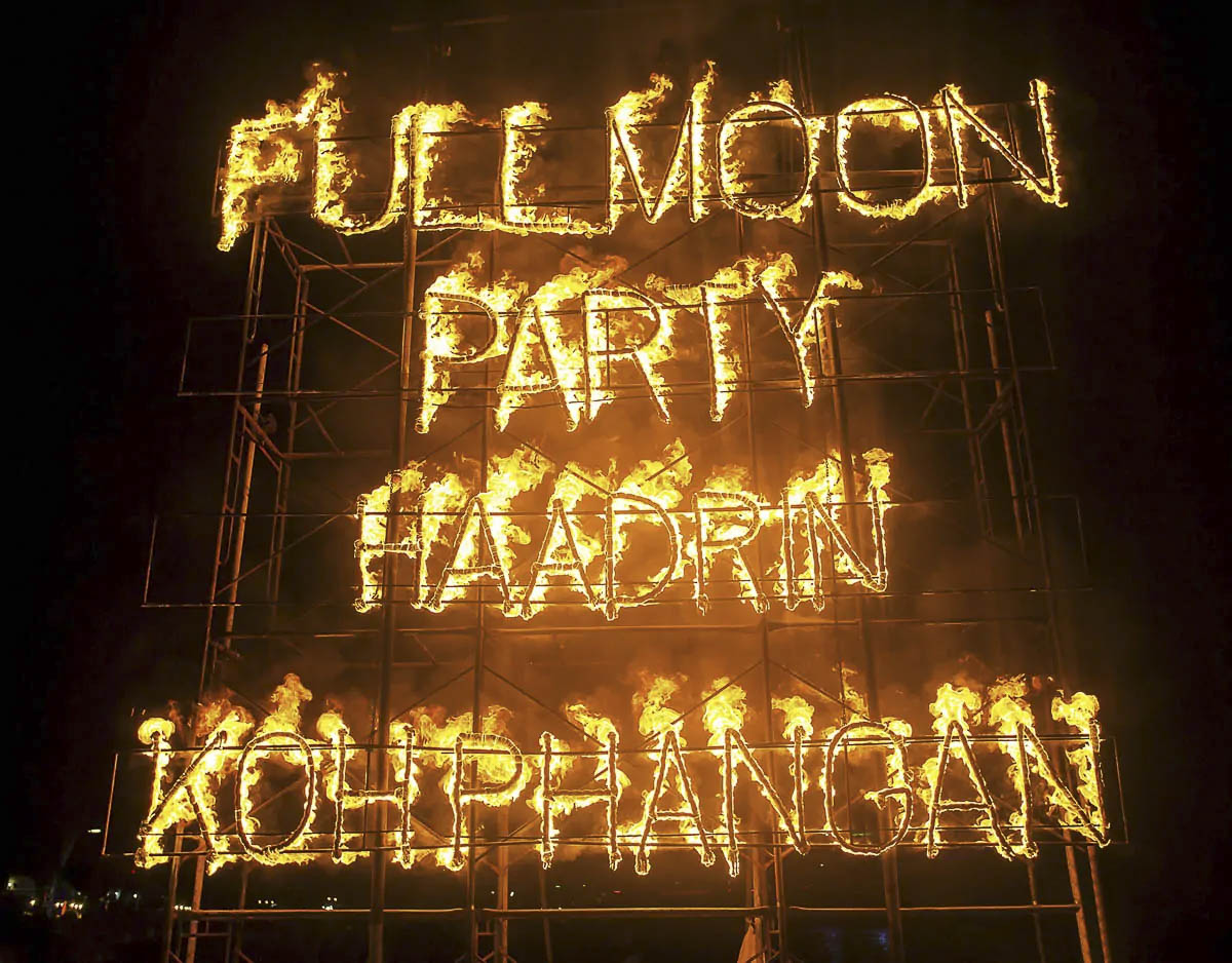 Estrutura com letreiro em chamas escrito “Full Moon Party Haad Rin Koh Phangan” durante a festa da lua cheia na Tailândia.