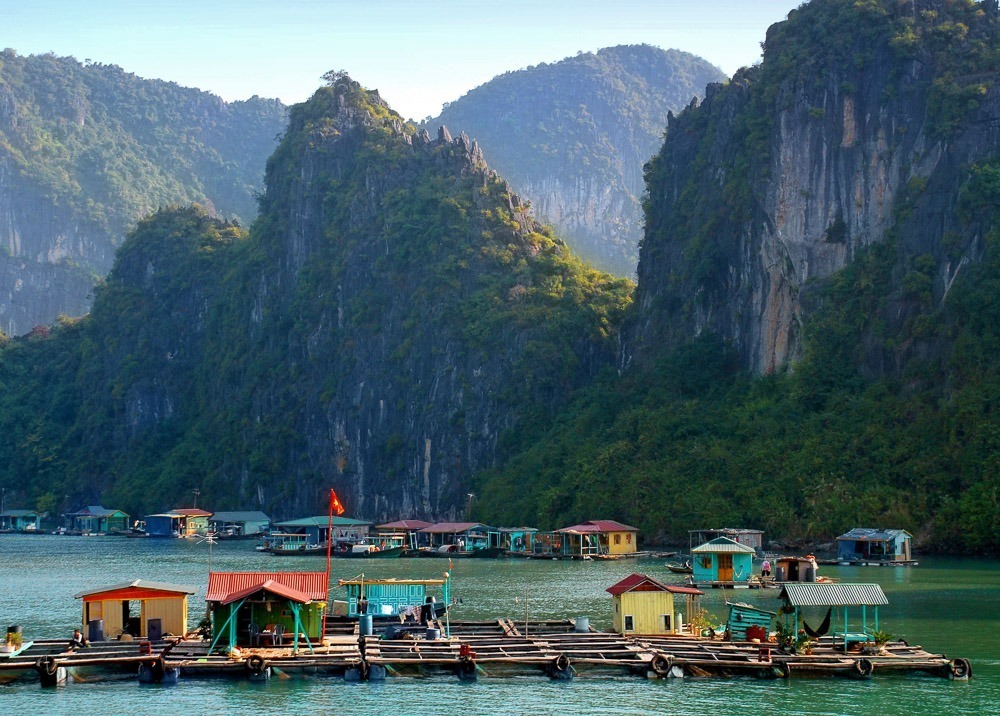 Casas flutuantes coloridas compõem uma vila sobre a água entre montanhas da Baía de Ha Long.