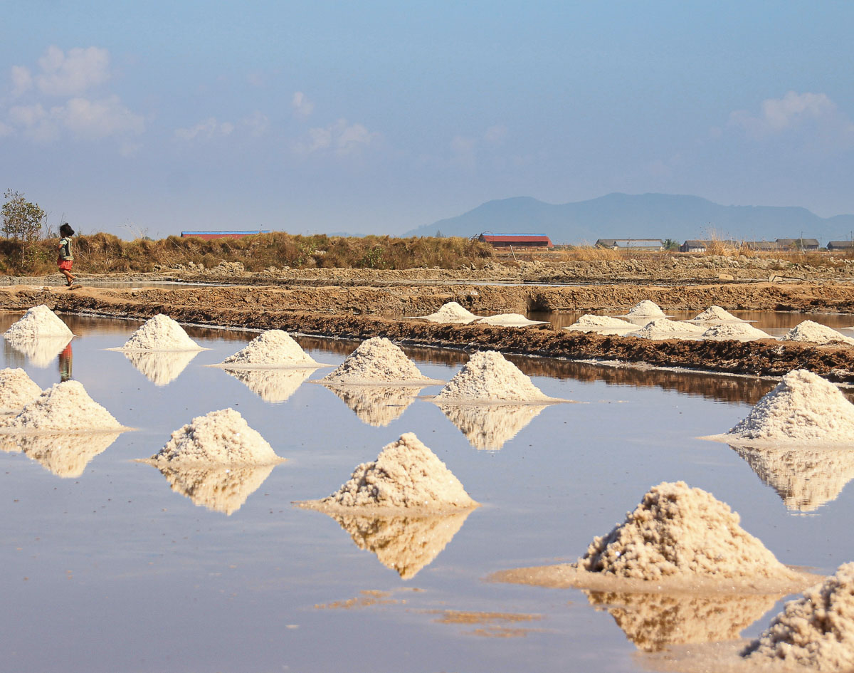 Campos de sal em Kampot com montes de sal refletidos na água sob céu azul.