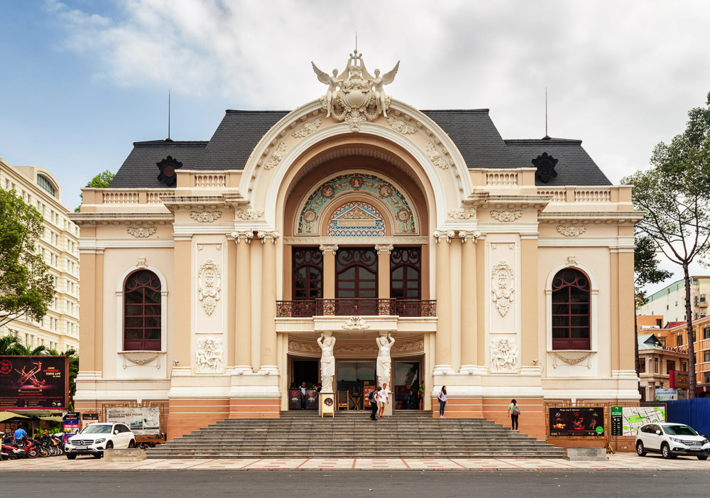 Entrada principal da Ópera de Saigon, com fachada francesa ornamentada e escadaria larga.