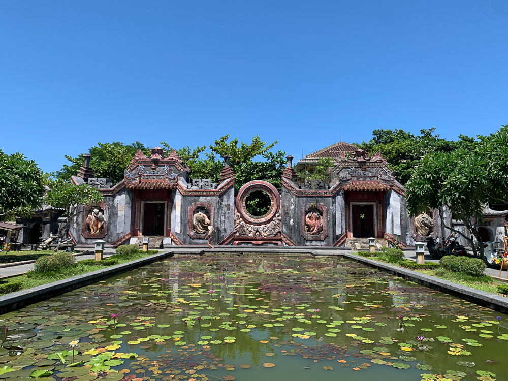 Templo ornamentado em Hoi An refletido em um espelho d'água com plantas.