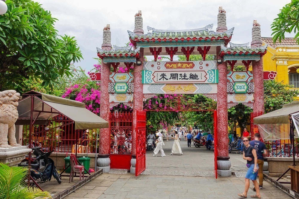 Portão colorido com inscrições em caracteres chineses na entrada de uma rua movimentada em Hoi An.