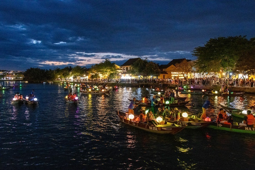 Barcos iluminados por lanternas coloridas flutuando à noite no rio de Hoi An durante um festival.