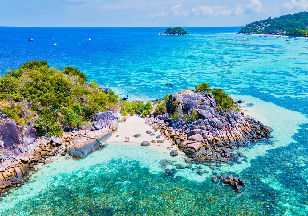 Pequena enseada entre rochas e vegetação em Koh Lipe com mar raso azul-claro.