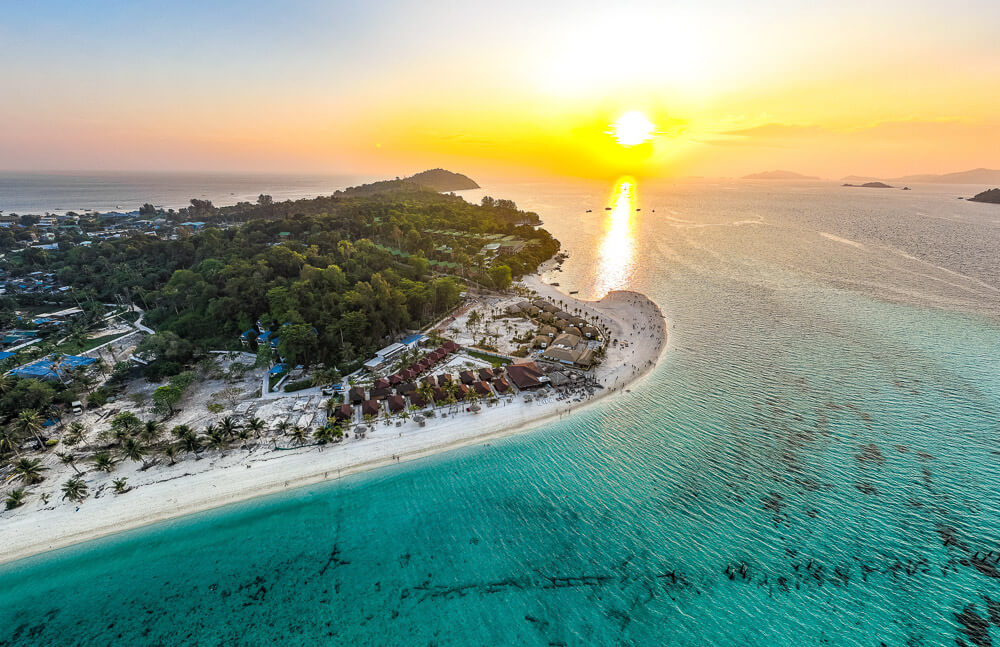 Nascer do sol dourado sobre a faixa costeira da praia Sunrise Beach em Ko Lipe, com o mar refletindo a luz.