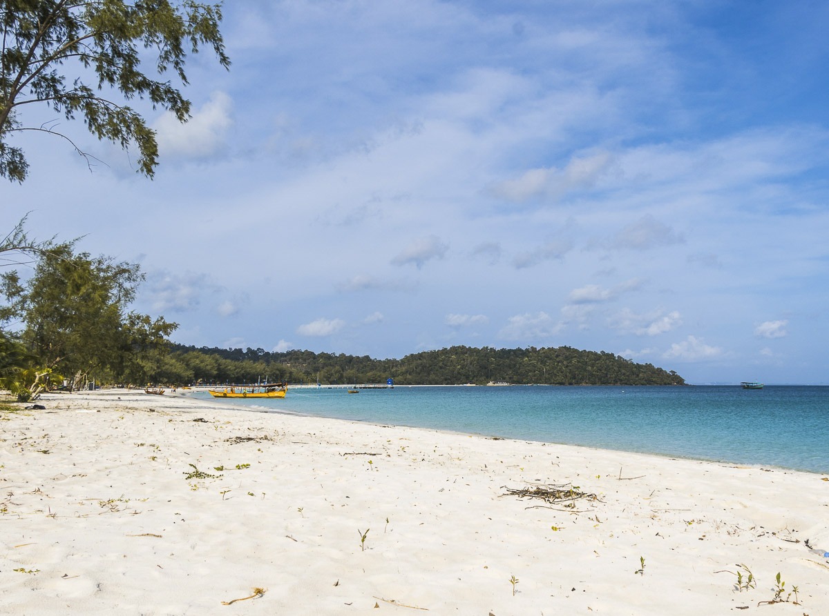 Praia de areia branca e mar azul-claro com barco amarelo em Koh Rong, Camboja.