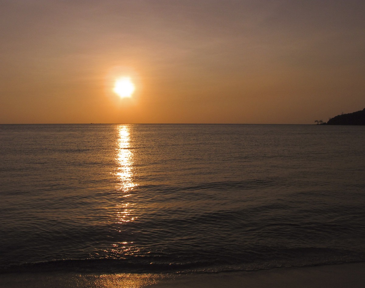 Pôr do sol alaranjado refletindo sobre o mar tranquilo em Koh Rong Sanloem.