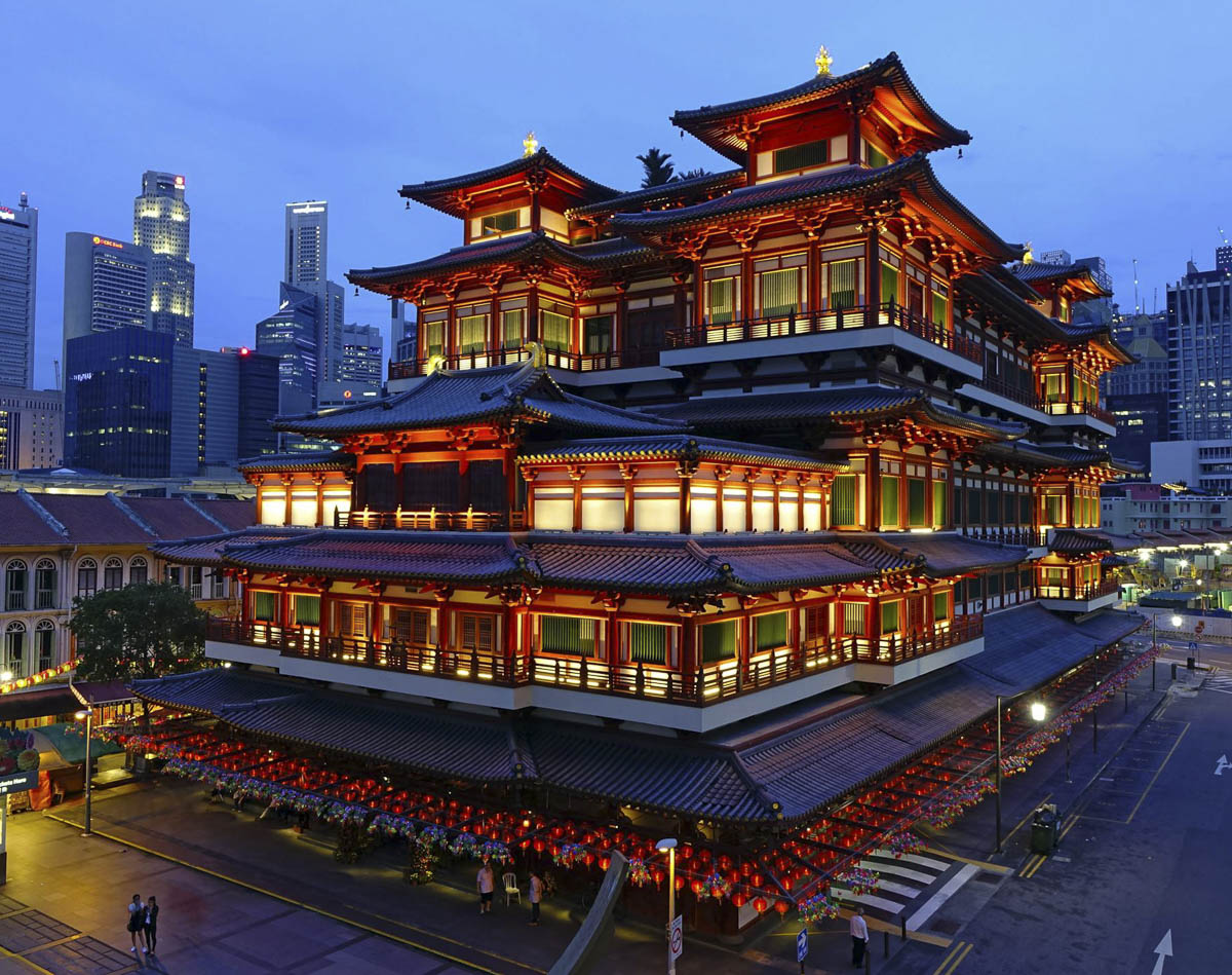 Templo Buddha Tooth Relic iluminado à noite em Chinatown, com arranha-céus ao fundo em Singapura.