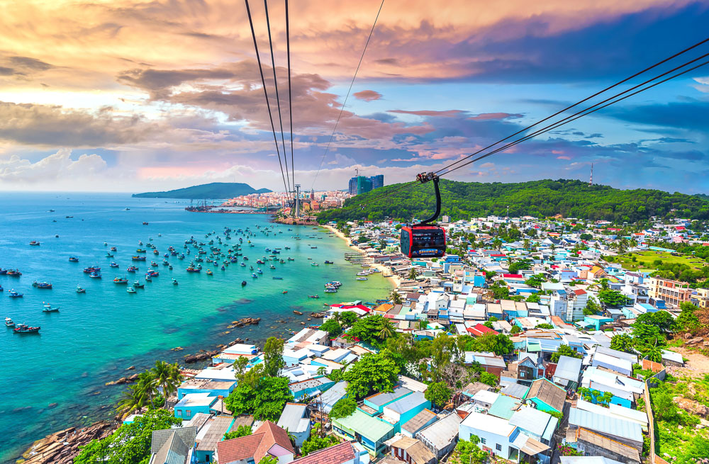 Vista aérea de Phu Quoc com teleférico sobre a costa e barcos no mar azul.