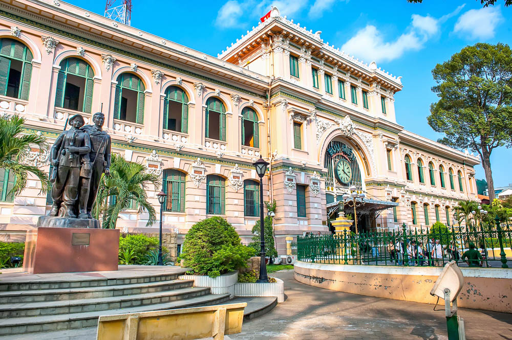 Fachada histórica do Central Post Office em Ho Chi Minh, com detalhes coloniais franceses e estátua na área externa.