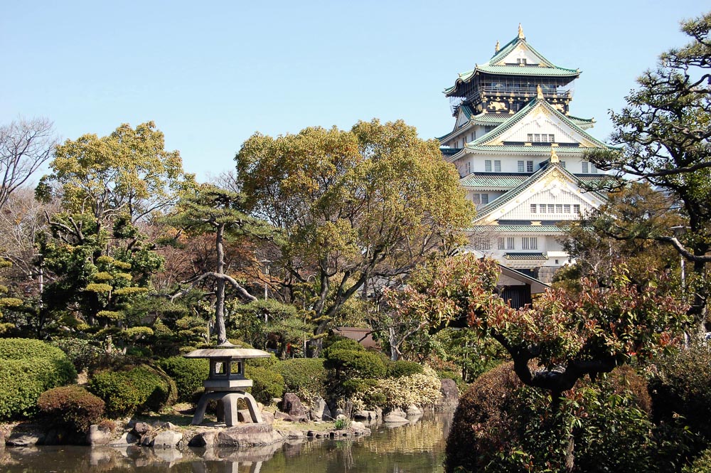 Cerejeiras em flor e jardim bem cuidado no Nishinomaru Garden, com o Castelo de Osaka ao fundo.
