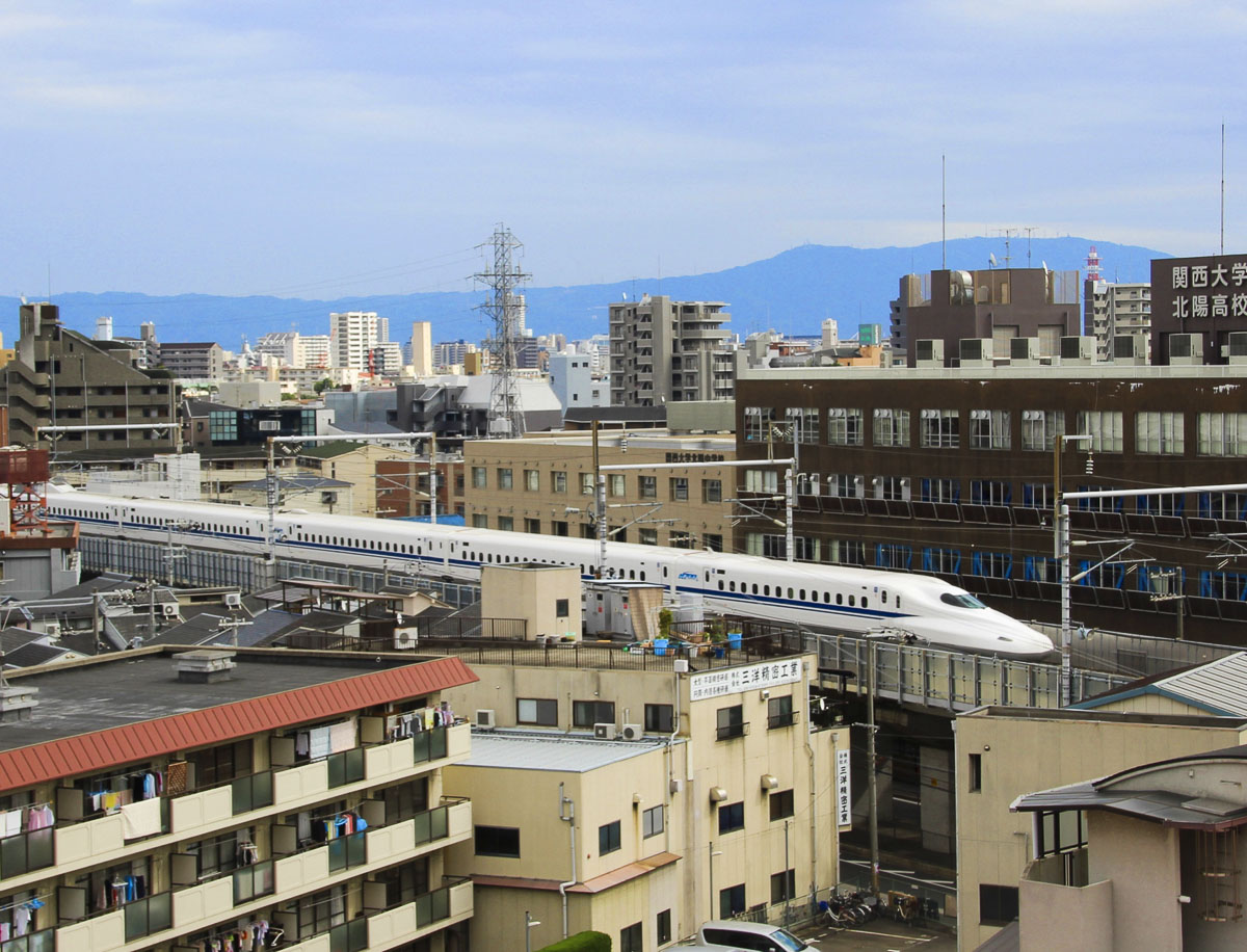 Trem-bala no Japão passando por uma área urbana, com prédios e montanhas ao fundo