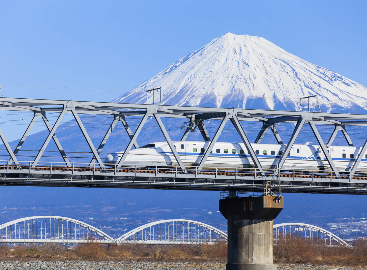 Trem-bala no Japão cruzando uma ponte metálica com o Monte Fuji ao fundo