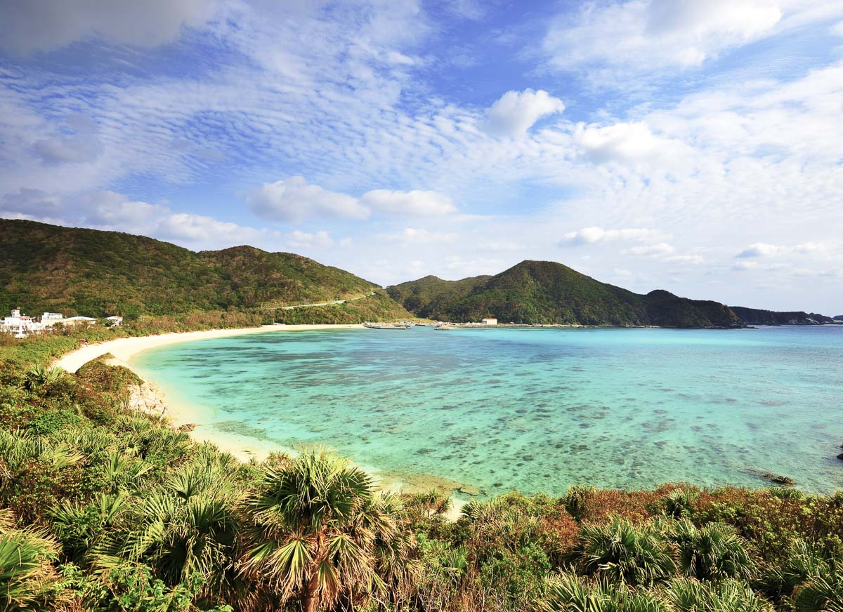 Praia tropical de Okinawa com mar azul-turquesa e vegetação.