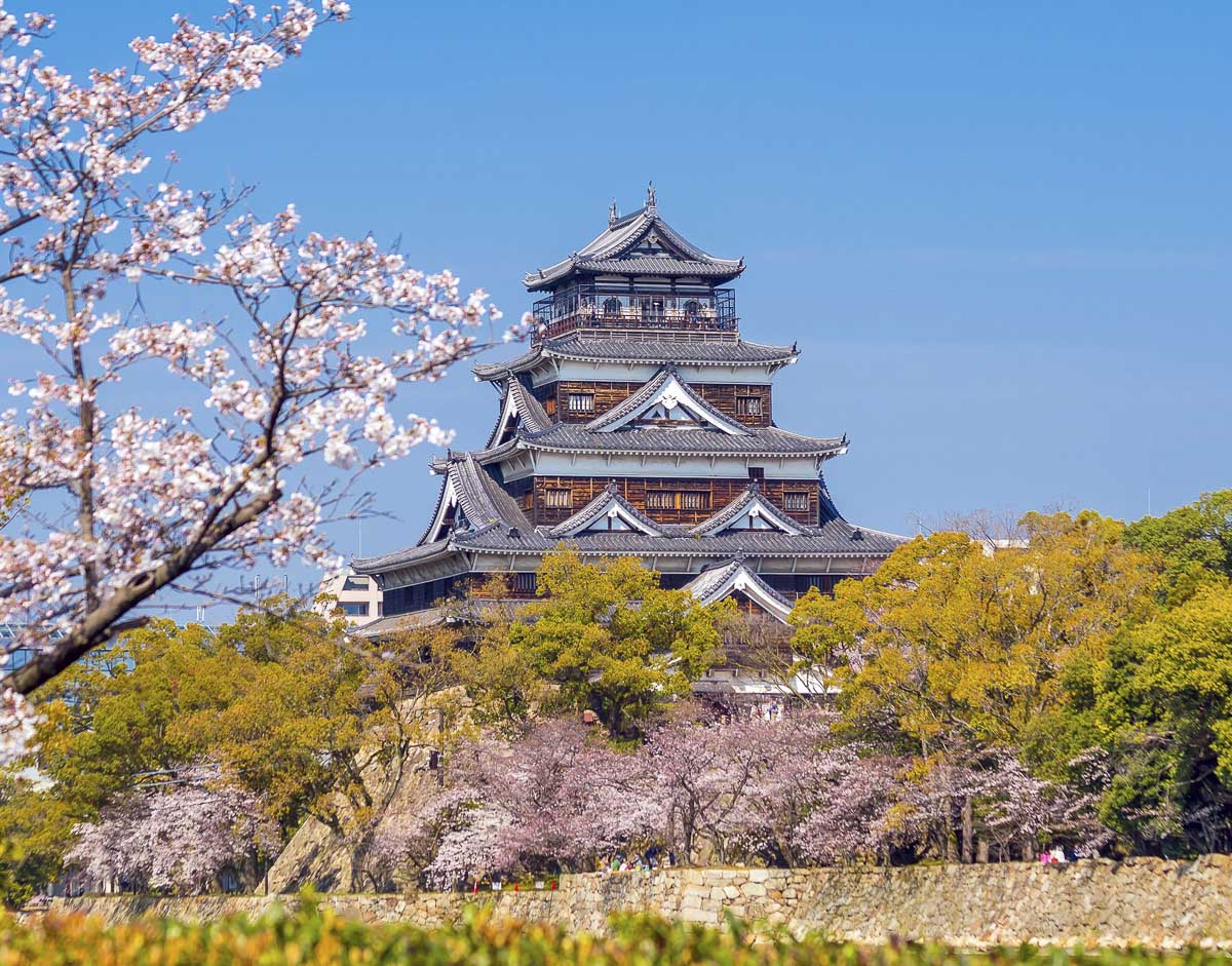 Castelo de Hiroshima cercado por árvores e flores de cerejeira.