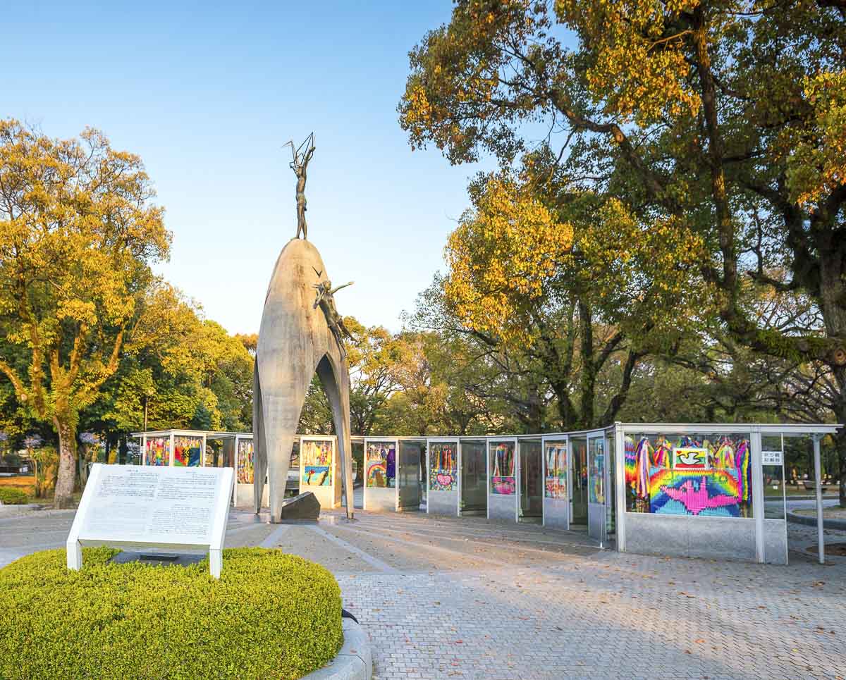 Monumento da Paz Infantil no Parque Memorial da Paz de Hiroshima, com escultura central e painéis coloridos ao fundo.