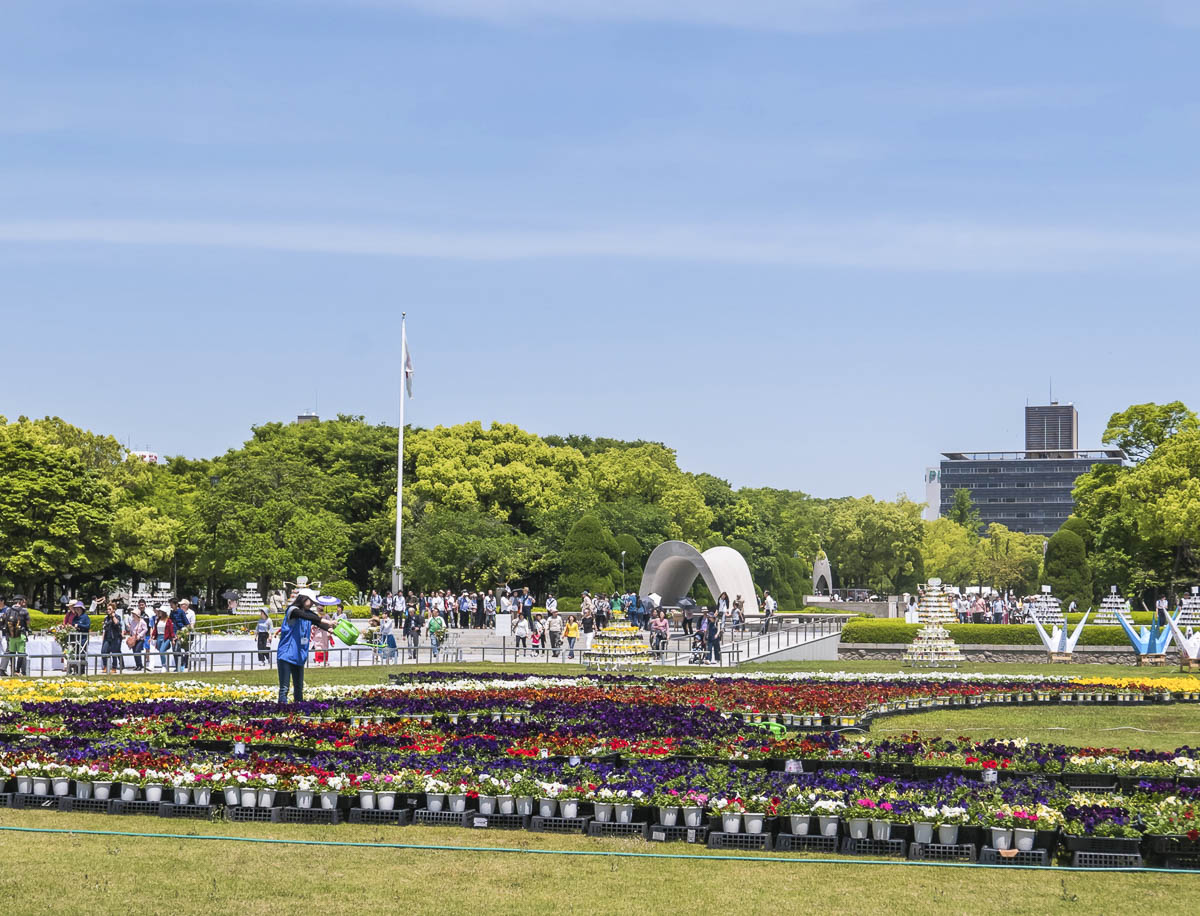 Área aberta do Parque Memorial da Paz de Hiroshima com canteiros floridos, visitantes e monumentos ao fundo